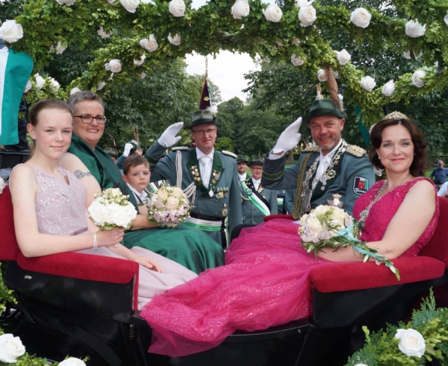  n der Königskutsche sitzen 2019 (von links) Edelmädel Jolie Täubert, Ehrendame Eva Göbel, Edelknabe Elias Schlüter sowie Frank und Nadine Täubert. Im Hintergrund grüßt  Zeremonienmeister Sebastian Tofall. Bild: Fotostudio Lichtblitz